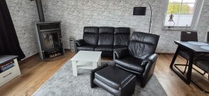 Gemütliches Wohnzimmer mit Sofa, Fernsehsessel mit Fußhocker und Kaminofen. - Bild 9: Nordsee Ferienhaus Dornumersiel strandnah - Hund willkommen - WLAN