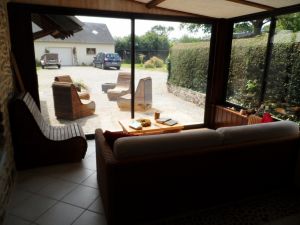 Der Wintergarten ist ausgestattet mit Rattancouch und kleinem Esstisch. Im Außenbereich ein weitere Sitzbereich und Blick auf Garten und unsere Garage. - Bild 10: Les Prunelles Normannisches Natursteinhaus mit Wintergarten und Kamin