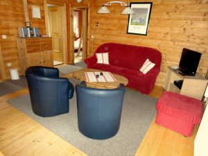 Vom Wohnzimmer aus gelangt man in sämtliche Räume des Hauses. Neben der Sitzgarnitur mit Couchtisch steht der Flachbildschirm des SAT-Anschlusses und im darunter befindlichen Schrank Videorekorder und DVD-Player. - Bild 1: Blockhausurlaub Bayerischer Wald - ideal für Familien mit Kindern und Hund