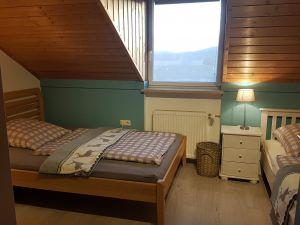 Schlafzimmer mit zwei Einzelbetten, Schrank und Tisch. Zum Schlafzimmer gehört eine separate Toilette mit Waschbecken. - Bild 19: Urlaub im gemütlichen Ferienhaus Waldhäuschen Zandt- Bayerischer Wald