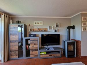 Offene Küche. Wohnzimmer mit Schlafcouch für zwei Personen und Couchtisch, Wohnzimmerwand, Esstisch mit Sitzbank und drei Stühlen, Kaminofen. Zur Unterhaltung stehen ein Flachbild-TV mit Sat-Empfang, ein DVD-Player und ein Radio zur Verfügung. - Bild 7: Urlaub im gemütlichen Ferienhaus Waldhäuschen Zandt- Bayerischer Wald