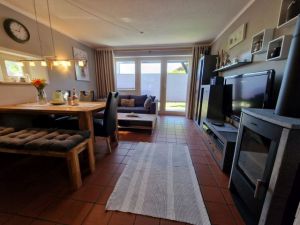 Offene Küche. Wohnzimmer mit Schlafcouch für zwei Personen und Couchtisch, Wohnzimmerwand, Esstisch mit Sitzbank und drei Stühlen, Kaminofen. Zur Unterhaltung stehen ein Flachbild-TV mit Sat-Empfang, ein DVD-Player und ein Radio zur Verfügung. - Bild 5: Urlaub im gemütlichen Ferienhaus Waldhäuschen Zandt- Bayerischer Wald