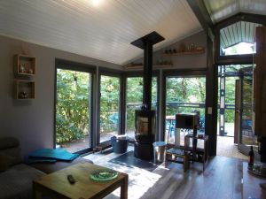 Wohnzimmer mit freistehenden Kaminofen und bodentiefe Fenster mit Blick in den Garten - Bild 2: Ferienhaus Mau & Wau - Waldhessen